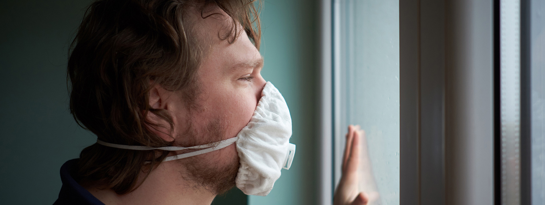 Man wearing a face-mask looking out of a window.