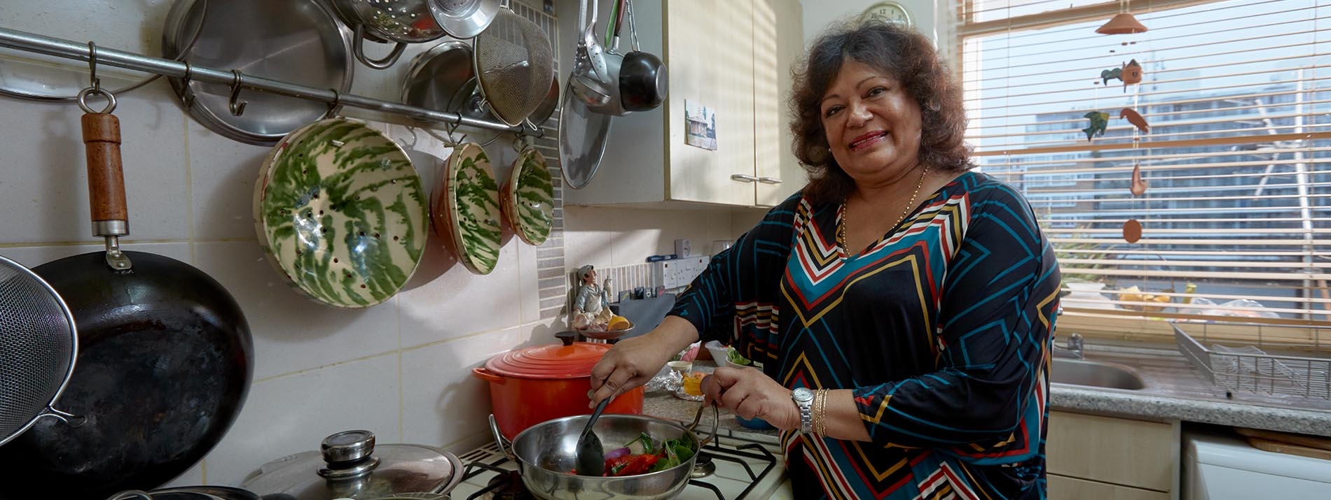 Μια γυναίκα που στέκεται στην κουζίνα της τηγανίζοντας λαχανικά.