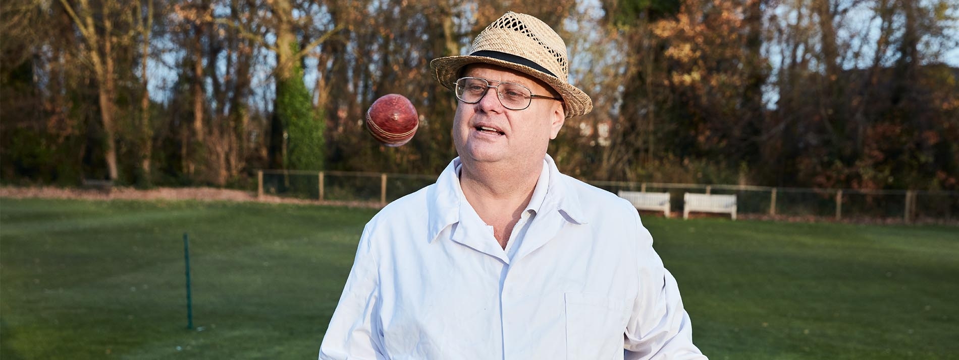 Ένας άντρας που φοράει γυαλιά και ψάθινο καπέλο, και κοιτάζει μια μπάλα η οποία πετά στον αέρα.