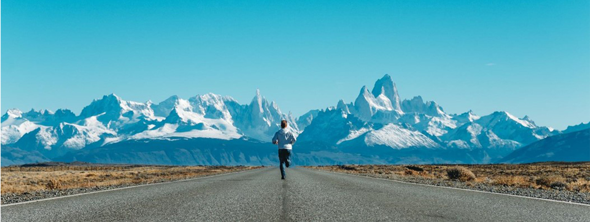 Man running in the middle of a desert road with snowy mountains in the background.