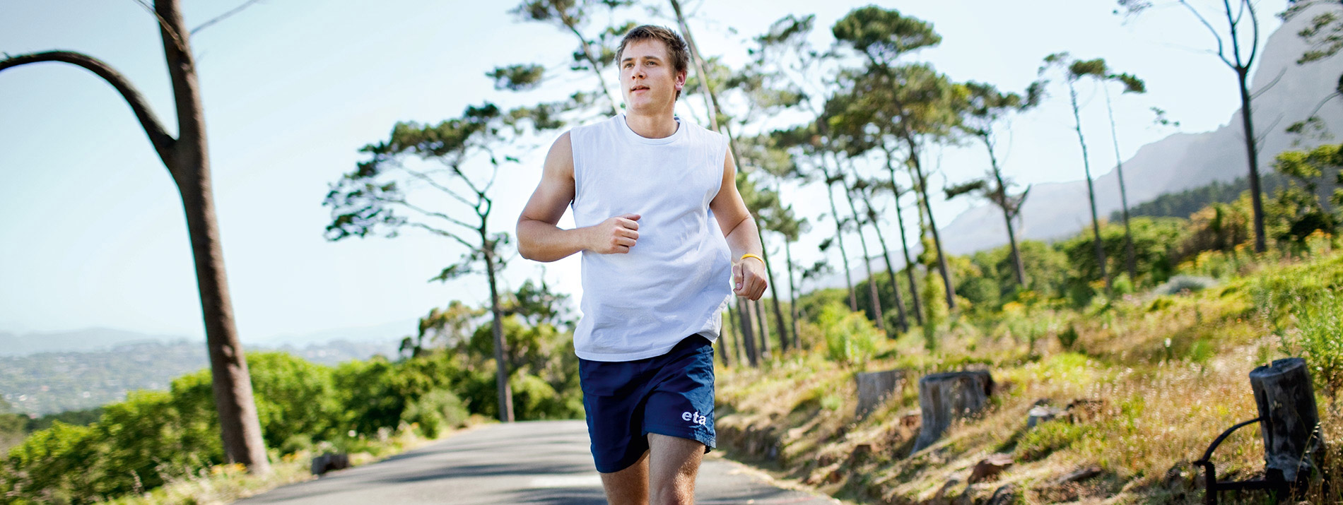 Man running in the middle of a road with mountains and vegetation in the background.