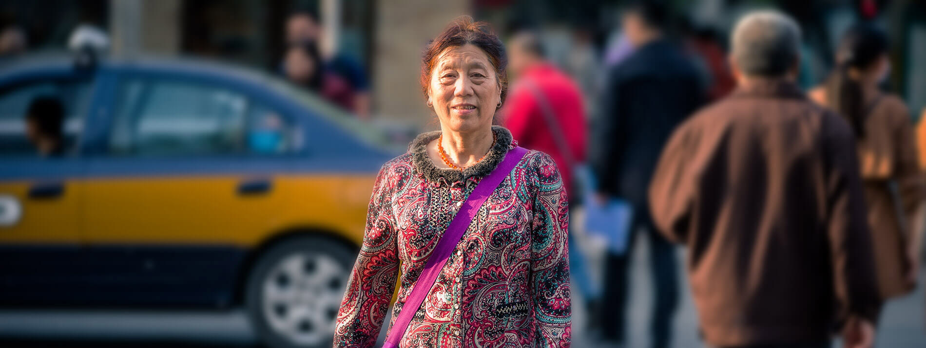 Woman walking in the street with people and a car passing by behind her.