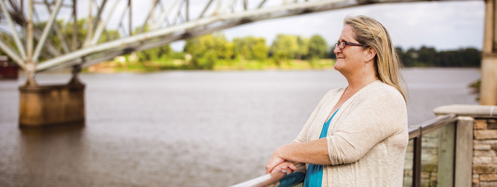 Woman standing next to a bridge looking out over a river