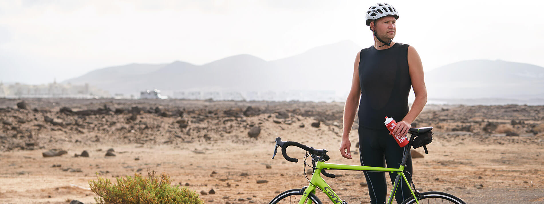 Man standing with his bike near a road with a desert in the background.