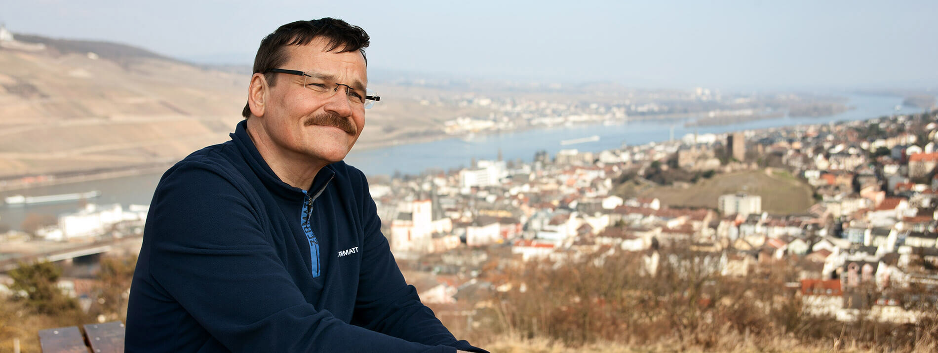 Man sitting on a hilltop with a city and river in the background.