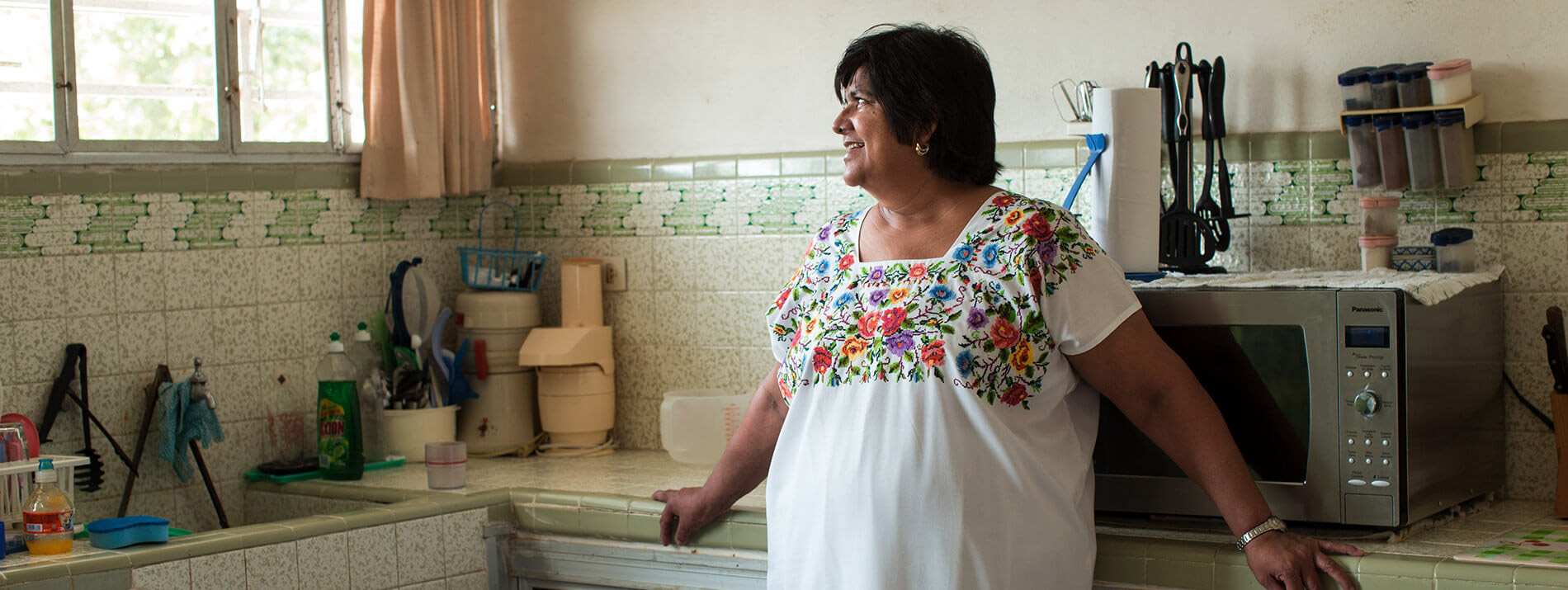 Smiling woman standing in a kitchen looking out the window.