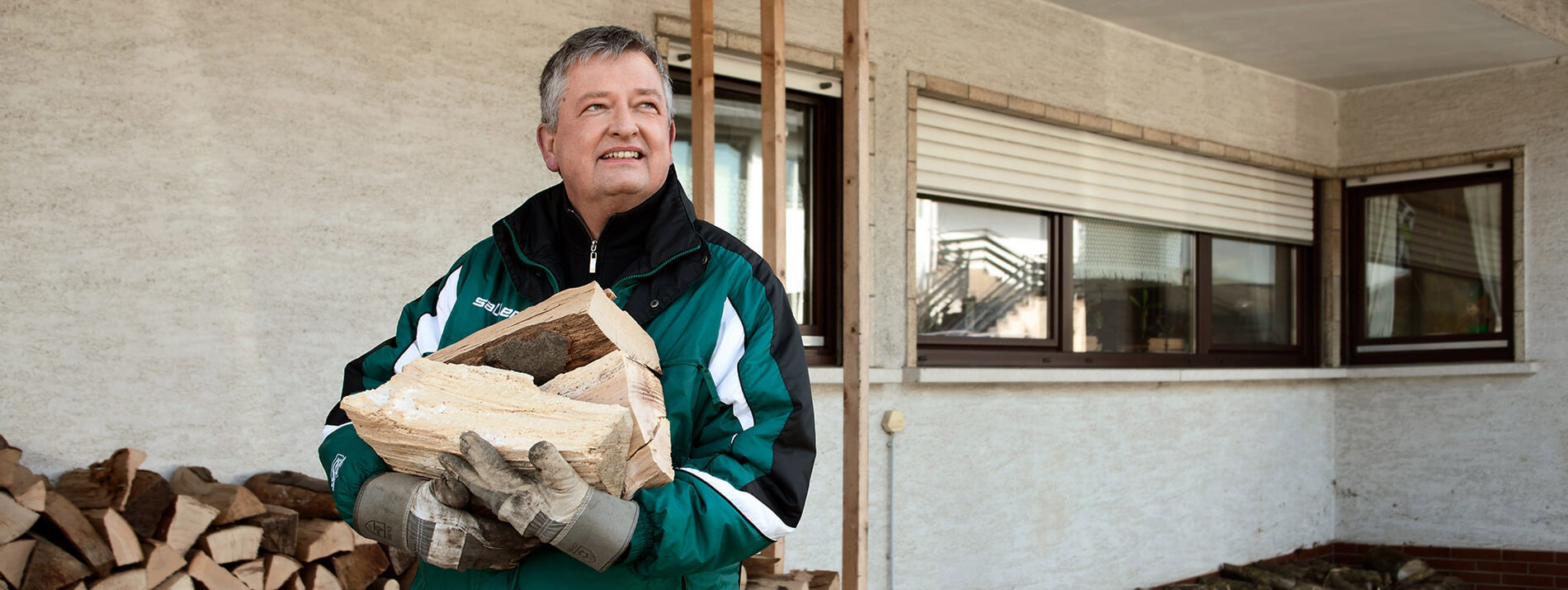 Man standing in front of a house carrying firewood.