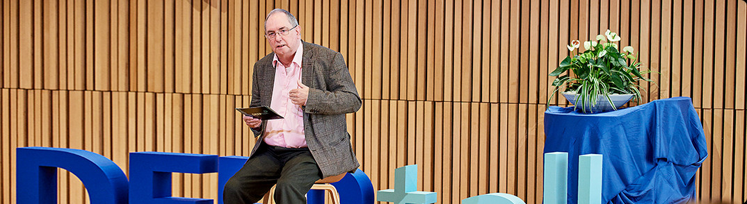 Man sitting a the stage holding a presentation.