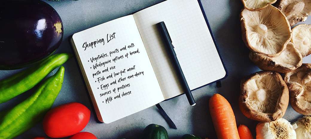 A shopping list laying next to various vegetables.